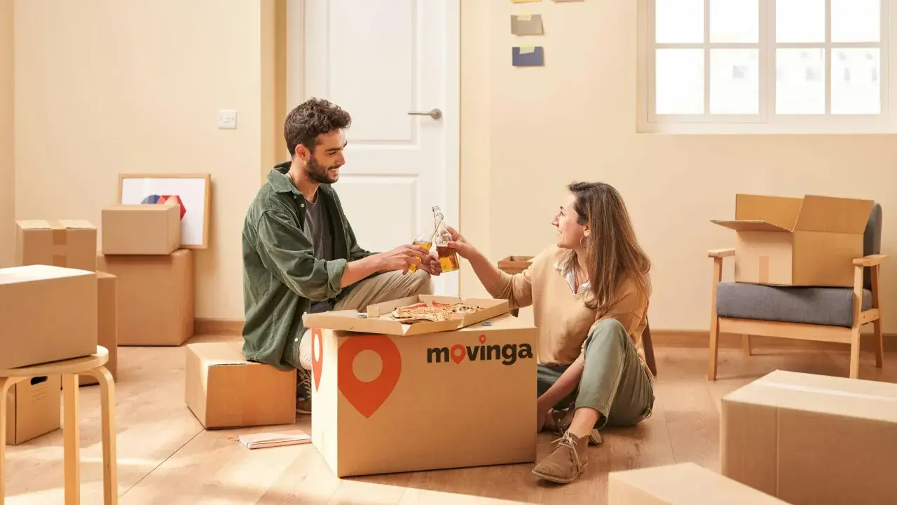 Un couple trinque avec des bouteilles devant une pizza, entouré de cartons. Un avis positif pour Movinga.