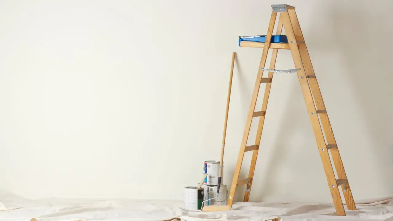 Préparation pour peindre une chambre : échelle en bois, pots de peinture, rouleau et bâton sur une toile de protection.