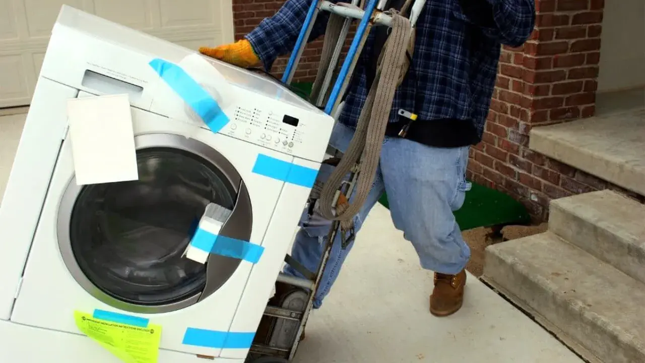 Un homme utilise un chariot pour comment monter une machine à laver dans les escaliers.