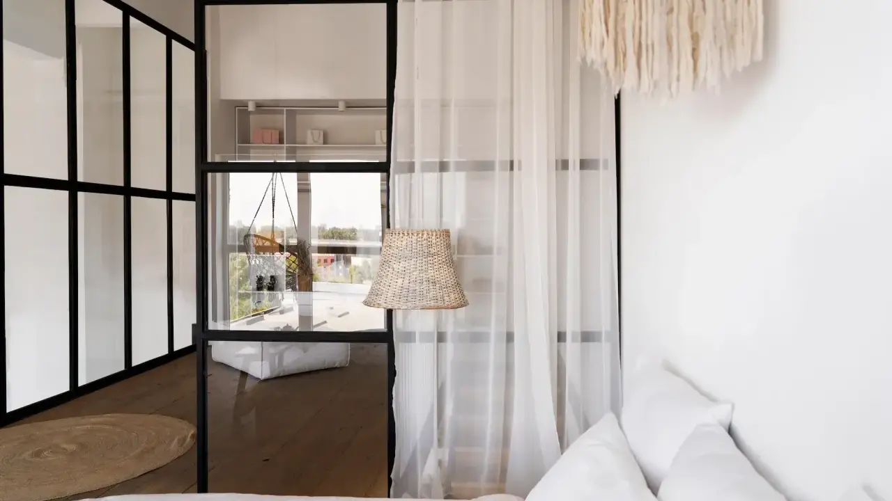 Verrière noire séparant une chambre en deux, avec une seule fenêtre visible. Un rideau blanc et un abat-jour en rotin ajoutent une touche cosy.