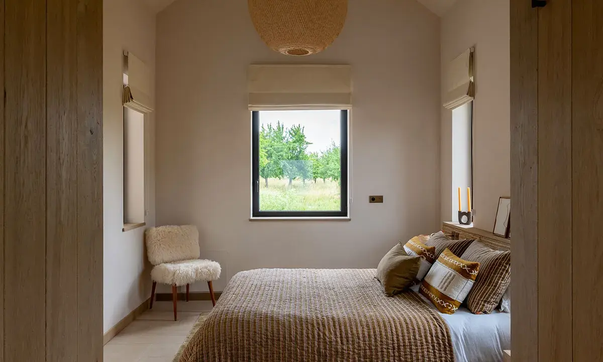 Aménagement petite chambre cosy avec lit douillet, fauteuil mouton et vue sur la nature.
