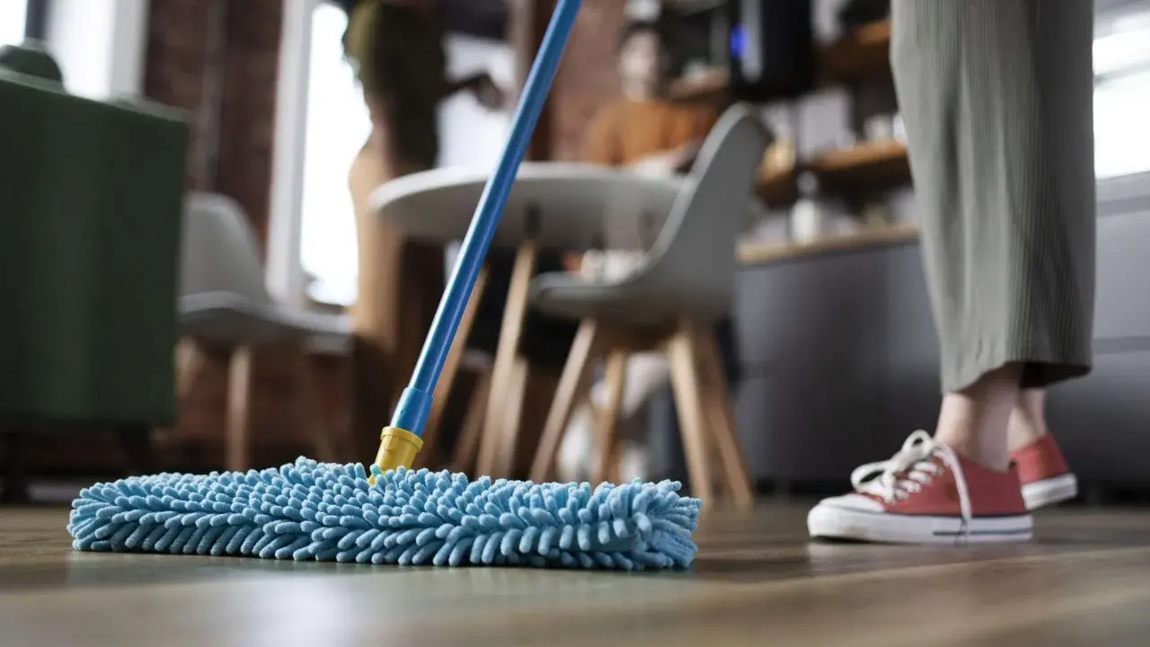 Nettoyage avant déménagement : une personne passe une serpillère bleue sur un parquet.