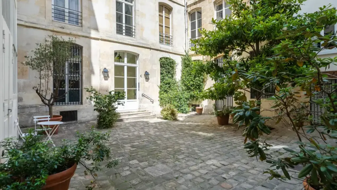 Cour pavée d'un immeuble parisien, avec un petit olivier et une table. Idéal pour un projet de déménager à Paris et profiter de la douceur de vivre.