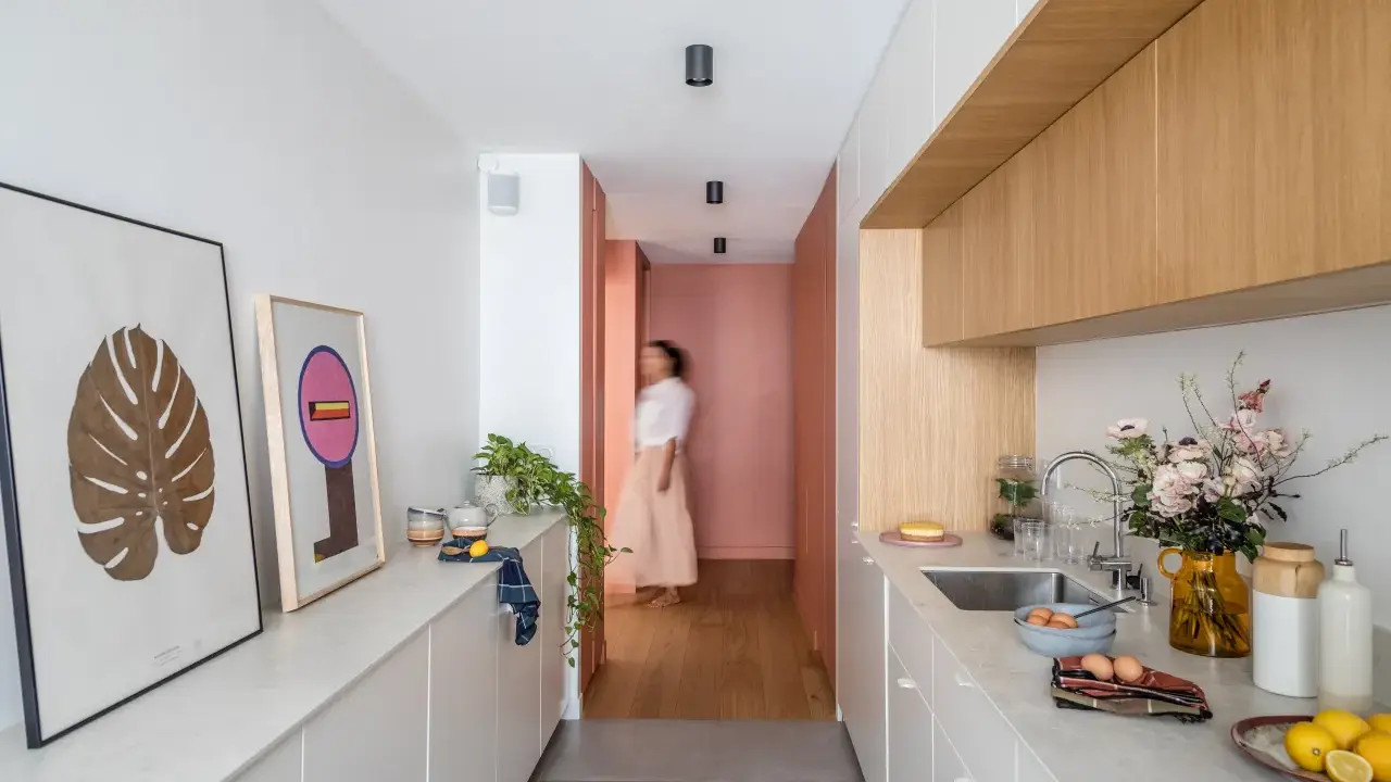 Cuisine moderne et lumineuse avec îlot central, décoration murale et personne marchant au fond.