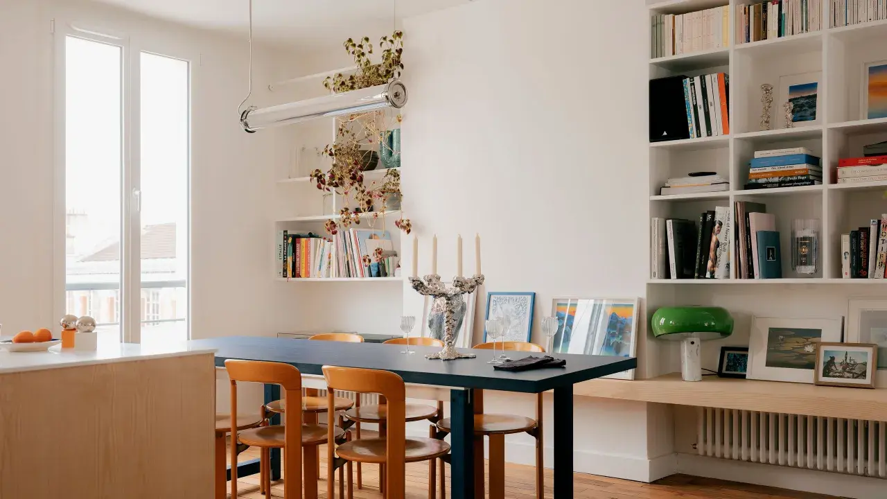 Salle à manger lumineuse d'un appartement traversant, avec table bleue, chaises en bois et étagères remplies de livres.