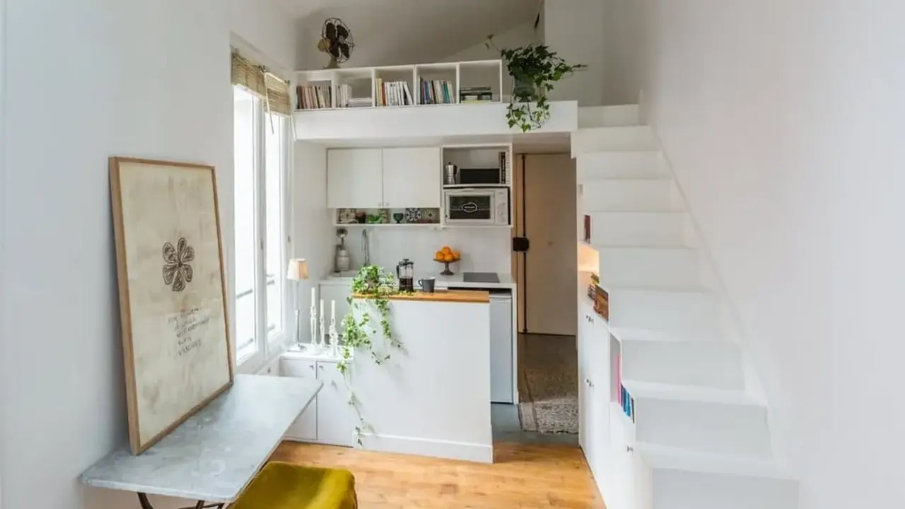 Un petit appartement optimisé avec une cuisine, un coin repas et un lit en mezzanine accessible par des escaliers blancs.