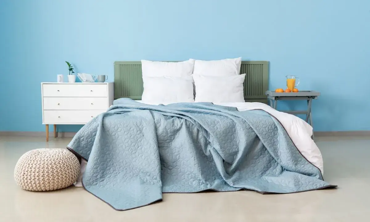 Une chambre paisible avec un lit douillet recouvert d'une couverture bleu glacier. Un pouf moelleux et une commode blanche complètent l'ensemble.