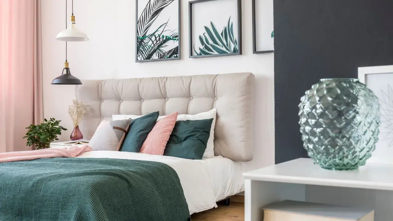 Une belle idée de tête de lit capitonnée, avec des coussins verts et roses, des plantes et des cadres botaniques.