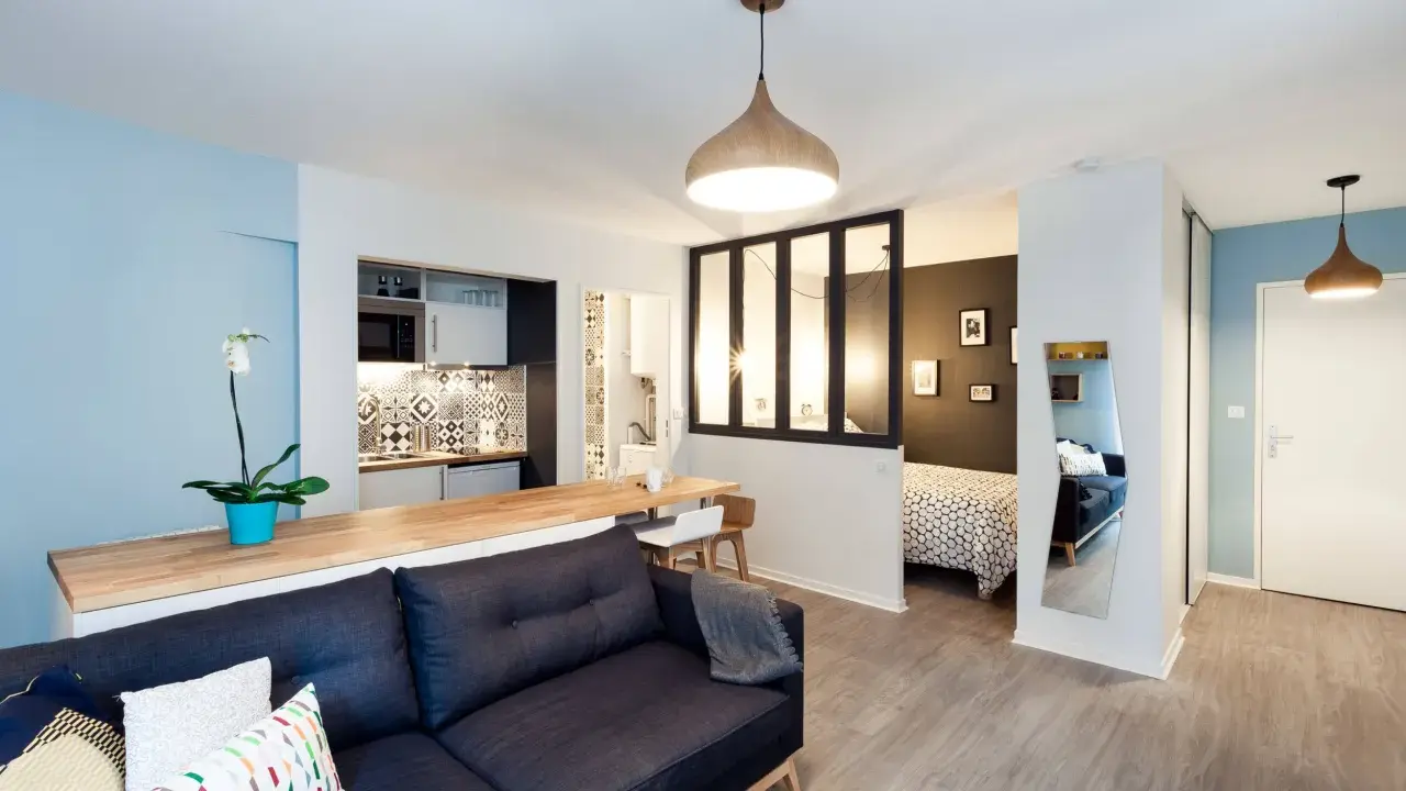 Aménagement studio 30m2 : salon cosy, cuisine moderne, coin repas et chambre séparée par une verrière.