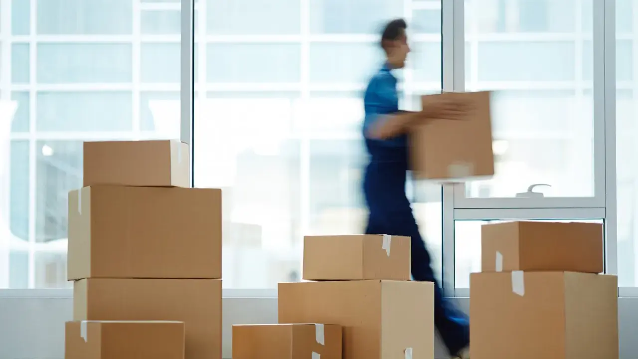 Un déménageur porte une boîte, entouré de cartons empilés. Une scène typique pour une facture déménagement.