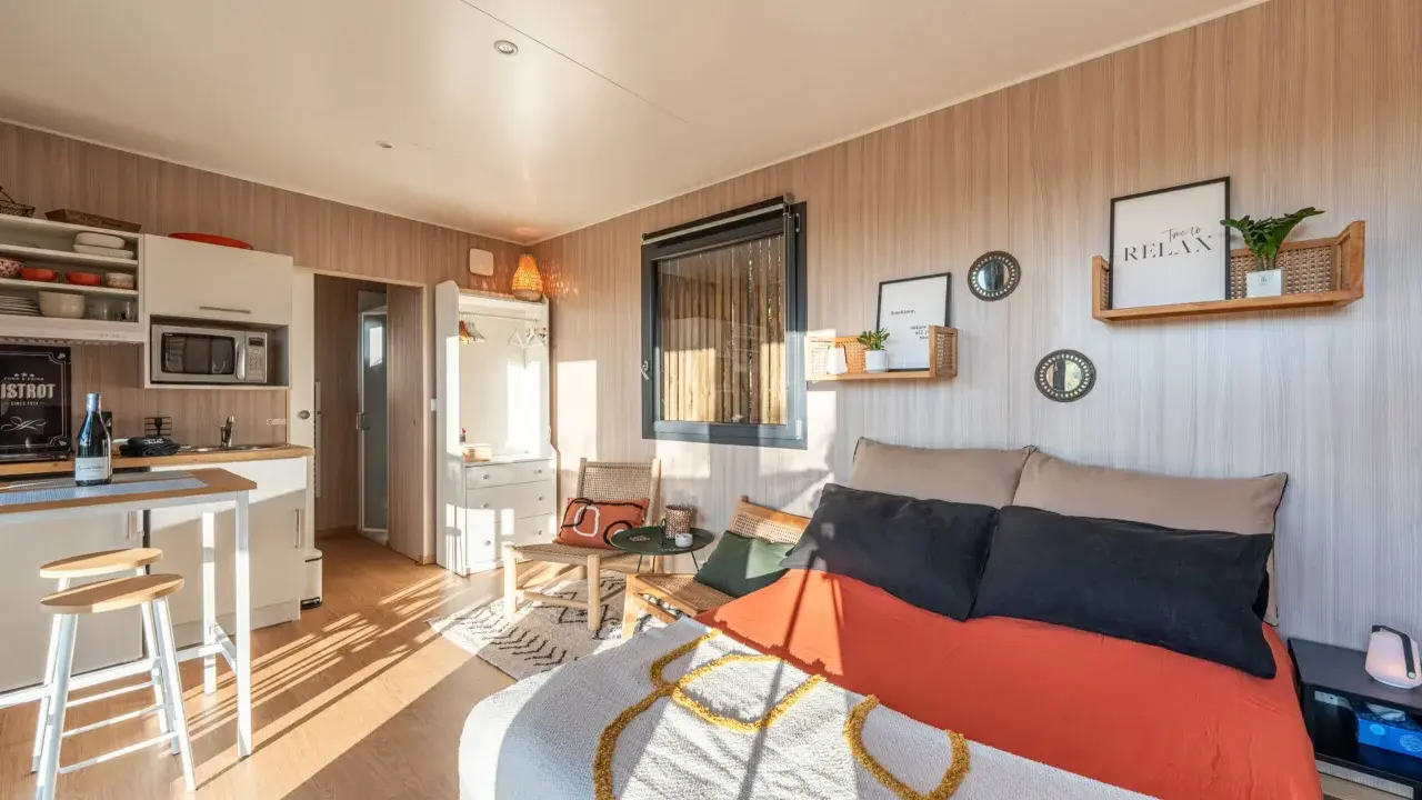 Aménagement d'un plan studio 20m2 en longueur : coin cuisine, lit confortable, fauteuils en rotin et décoration murale zen.