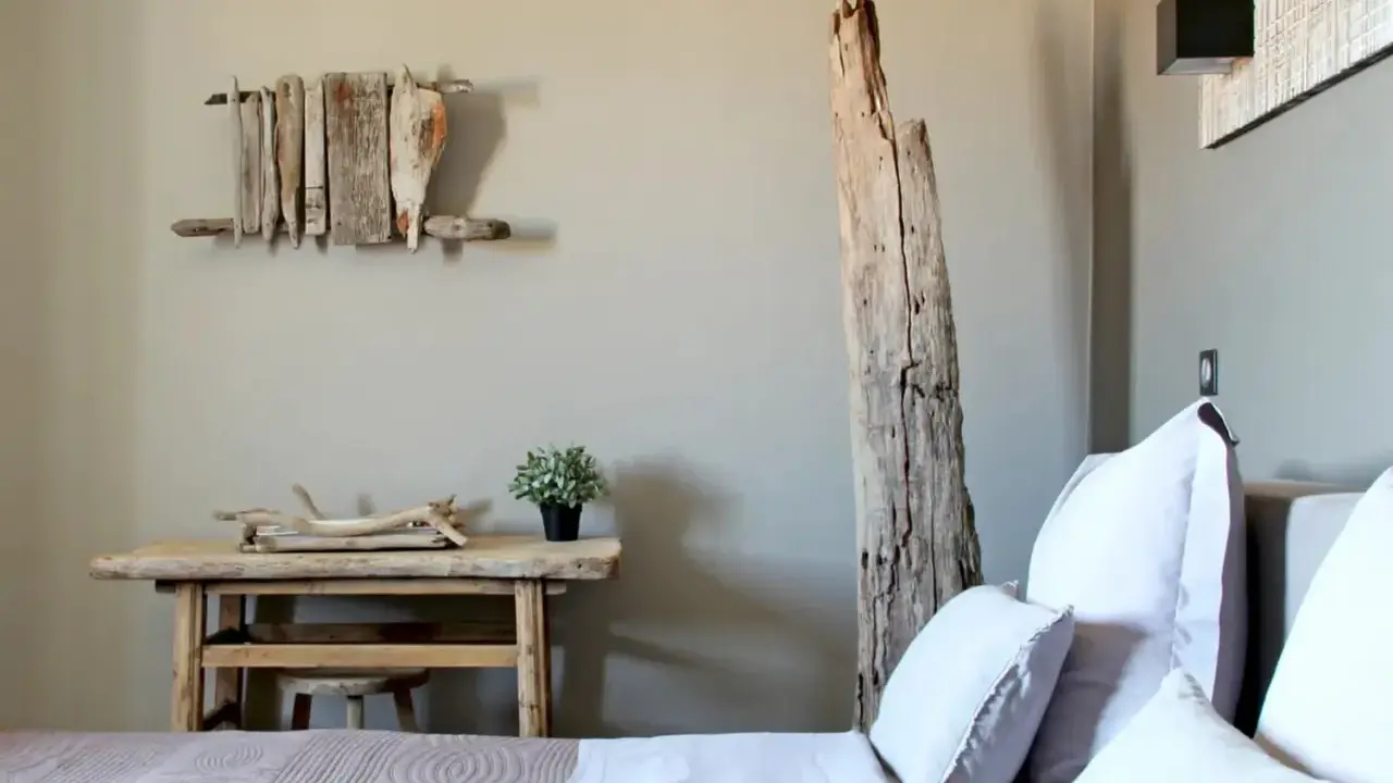 Idée pour comment décorer une chambre : un lit douillet, une table en bois brut, une plante verte et une sculpture murale en bois flotté.