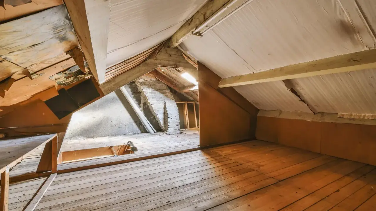Espace brut sous les toits, prêt à aménager un grenier. Planchers de bois, poutres apparentes et murs en briques.