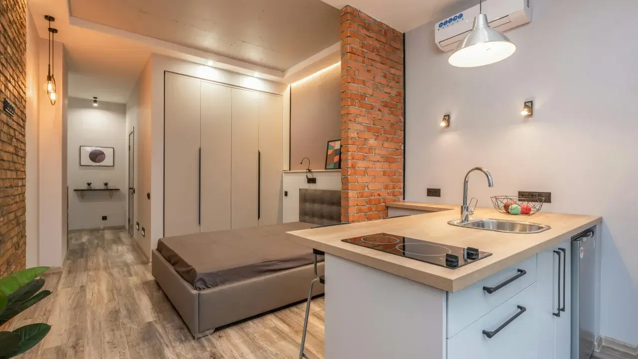 Aménagement studio 25 m2 : lit, cuisine équipée, rangements intégrés, mur en briques apparentes. Style moderne et fonctionnel.