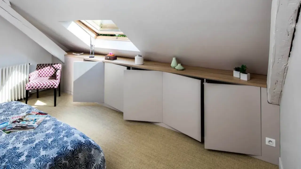 Chambre mansardée d'un coté avec lit, fauteuil à pois et rangements bas sur mesure. Un velux éclaire la pièce.