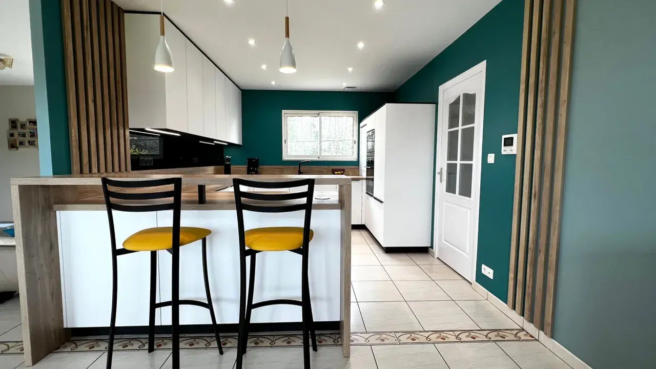 Cuisine moderne aux murs bleu canard, îlot central en bois, tabourets jaunes vifs. Une véritable inspiration cuisine pour des repas conviviaux.