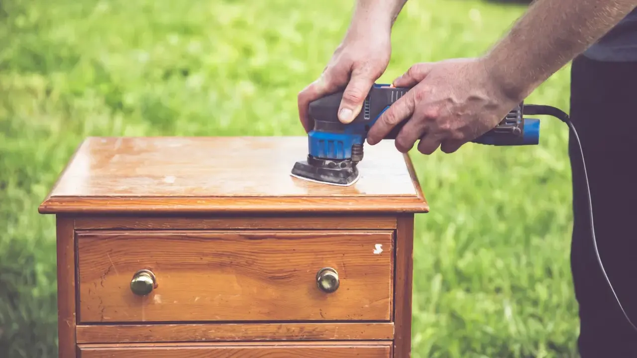 Préparation d'un meuble en bois : ponçage pour comment décaper un meuble en bois foncé. L'outil électrique enlève l'ancienne finition.
