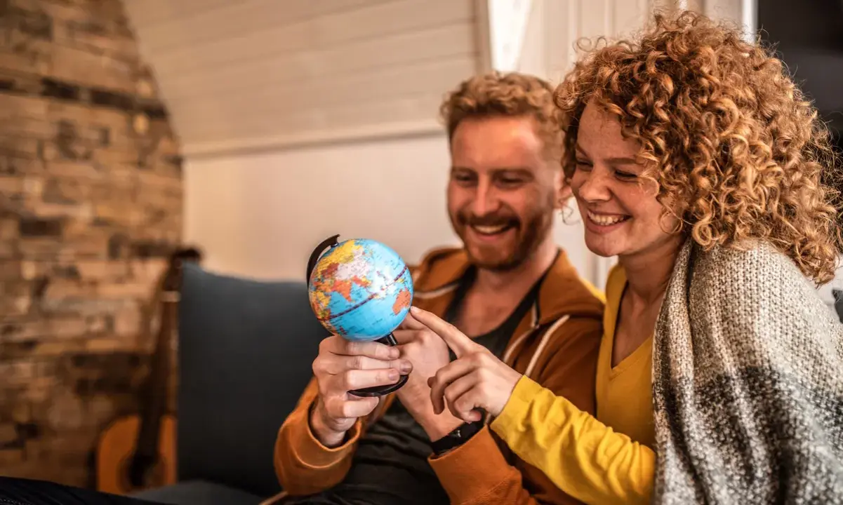 Couple souriant planifiant leur déménagement à l'étranger, pointant du doigt un globe terrestre.