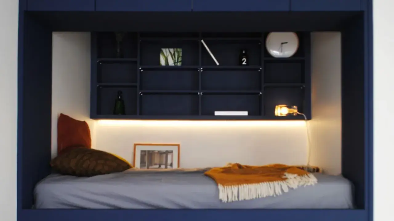Un lit confortable dans une alcôve bleue, avec des étagères remplies d'objets décoratifs. Parfait pour refaire sa chambre avec style.