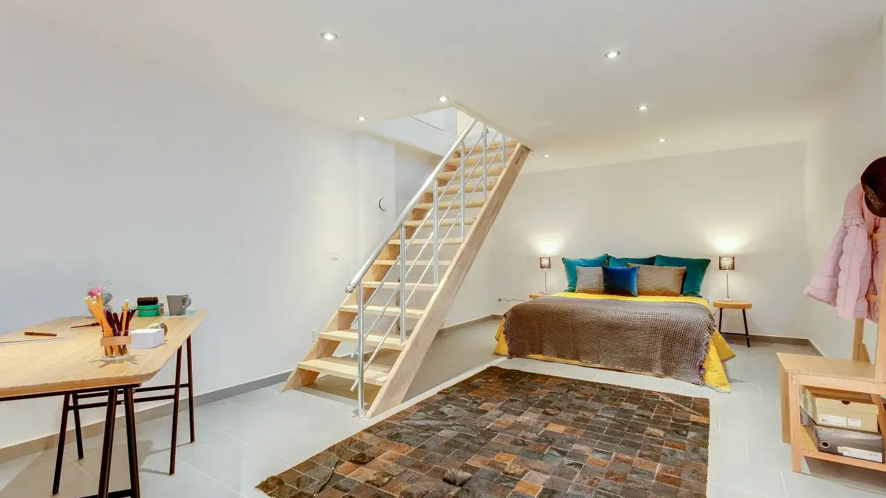 Aménager un sous-sol en pièce habitable : un lit douillet, un bureau fonctionnel et un escalier moderne créent un espace de vie confortable.