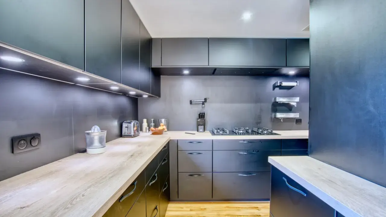 Cuisine moderne aux armoires sombres et plans de travail en bois. Une plaque de cuisson est installée, créant une cuisine sans hotte visible.