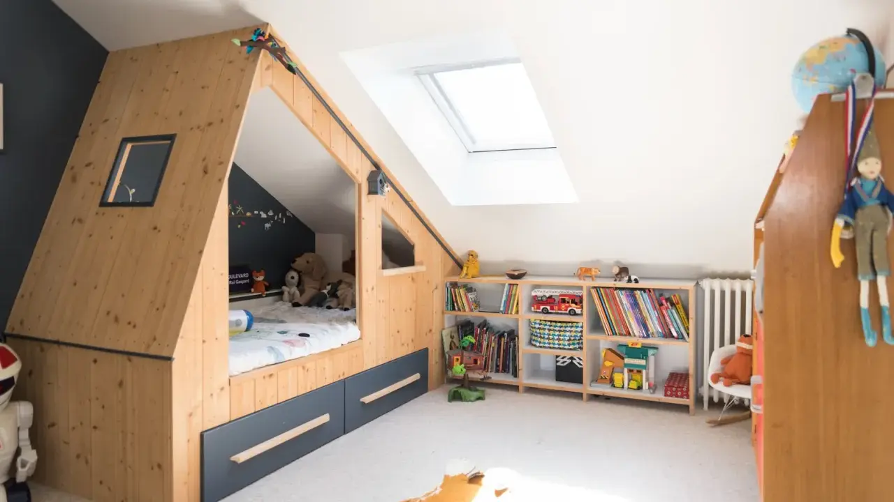 Chambre d'enfant aménagée sous les combles avec un lit cabane en bois, étagères remplies de jouets et livres. Un plan d'aménagement astucieux pour optimiser l'espace.