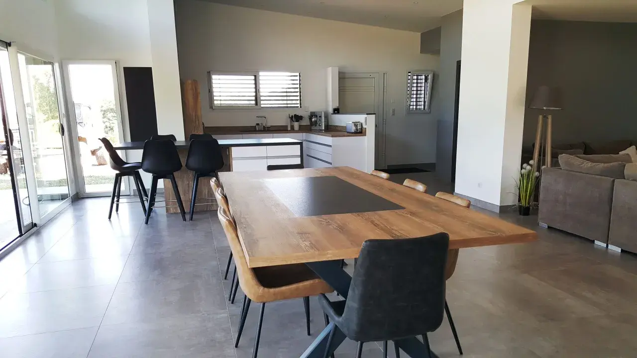 Grande cuisine ouverte sur salon, avec îlot central, table en bois et chaises modernes.