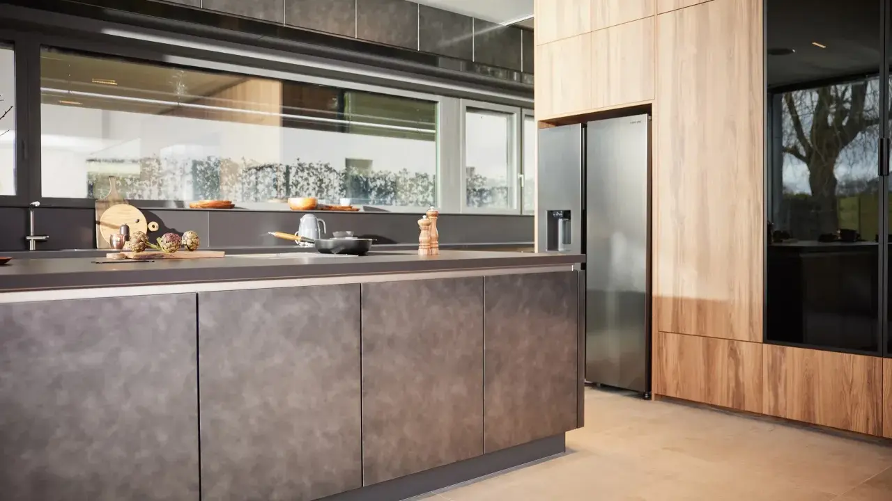 Une cuisine en plan moderne avec des armoires en bois et des surfaces sombres. Un réfrigérateur en acier inoxydable est visible.