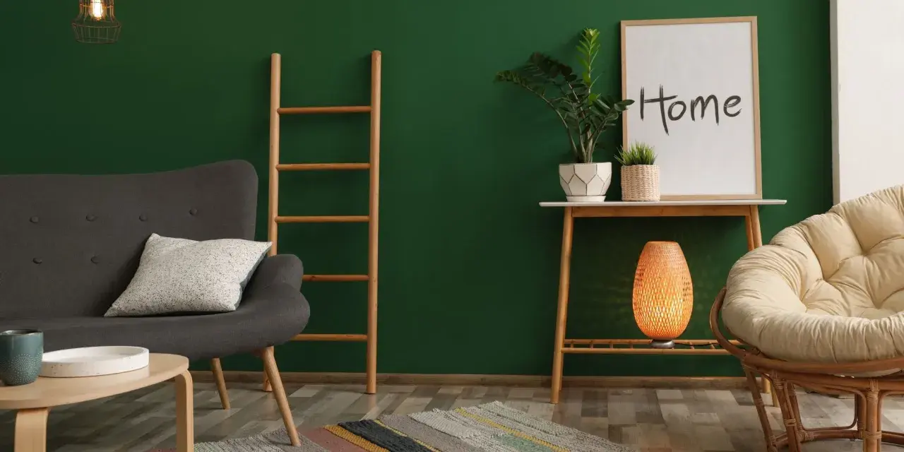 Un salon cosy avec un mur vert sapin, un fauteuil gris, une échelle en bois, une plante et un cadre "Home".