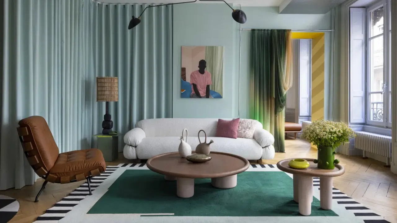 Un salon moderne avec un canapé blanc bouclé, un fauteuil en cuir marron, une table basse ronde et un tapis graphique. Une décoration appartement audacieuse et colorée.