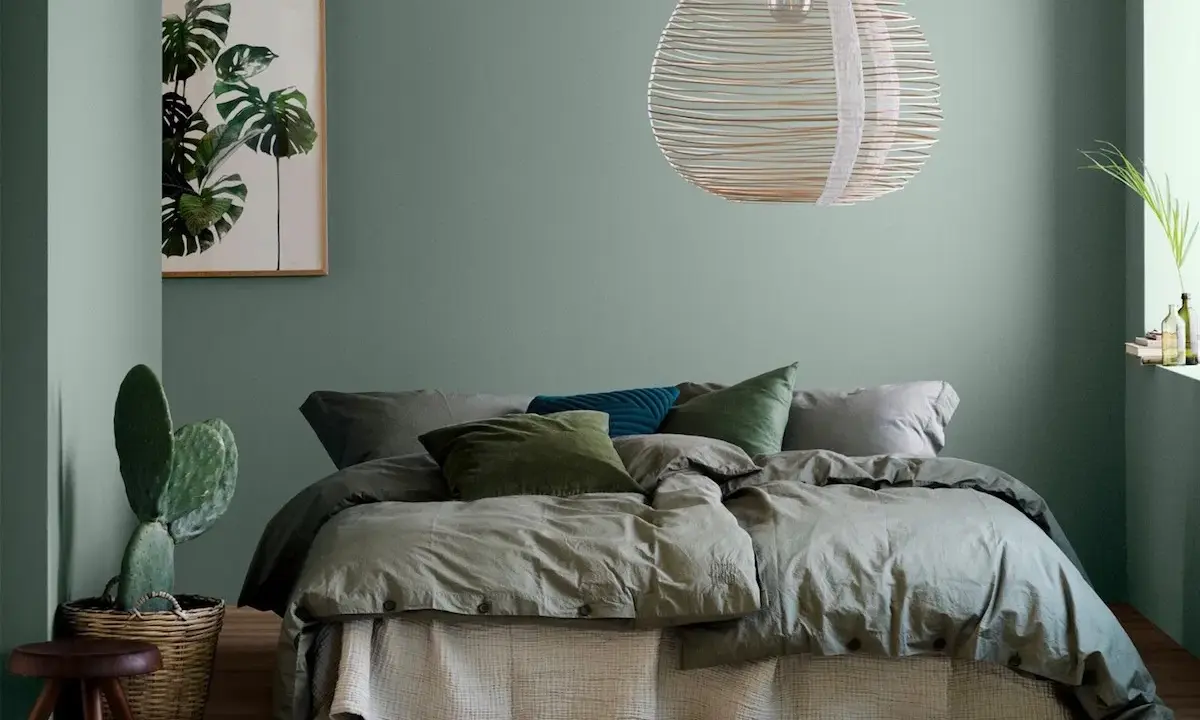 Une chambre vert sauge apaisante avec un lit douillet, un cactus et une œuvre d'art botanique.