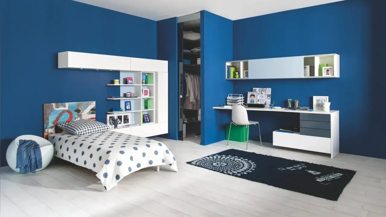 Chambre d'enfant moderne aux murs d'un profond **couleur bleu**. Un lit blanc à pois bleus, une étagère murale et un bureau complètent l'espace.