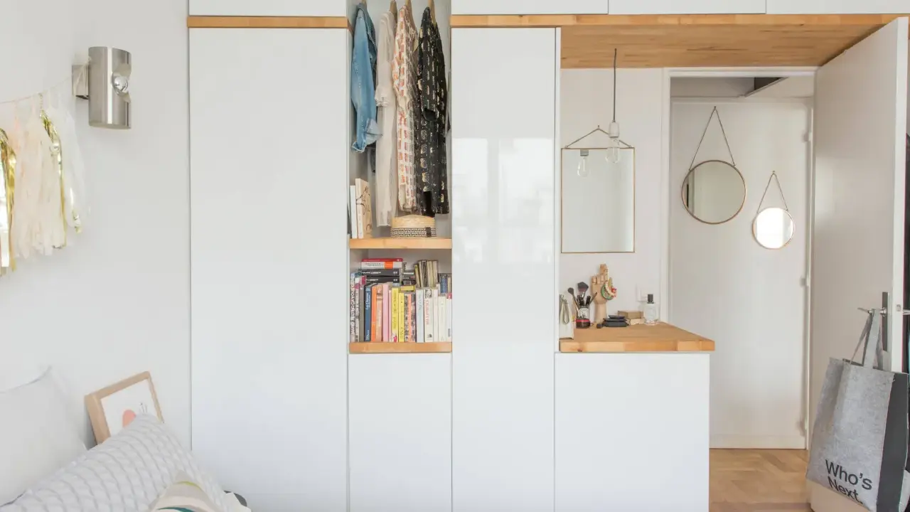 Chambre avec dressing intégré, organisée avec des étagères de livres et des vêtements suspendus. Un coin coiffeuse avec miroir et accessoires complète l'espace.