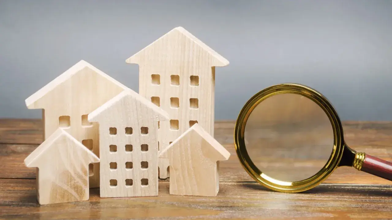 Maquettes de maisons en bois et une loupe, symbolisant la recherche pour trouver un logement rapidement.