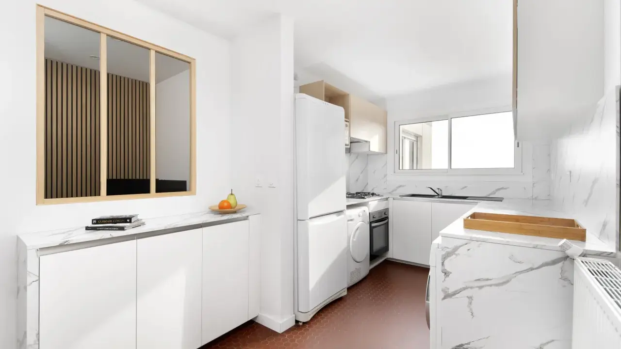 Relooker cuisine avant après : une cuisine moderne et lumineuse avec des meubles blancs, un plan de travail marbré et un sol hexagonal rouge.