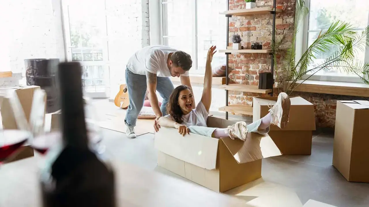 Un couple s'amuse en déménageant. Elle glisse dans un carton, un objet fragile, tandis qu'il la pousse.