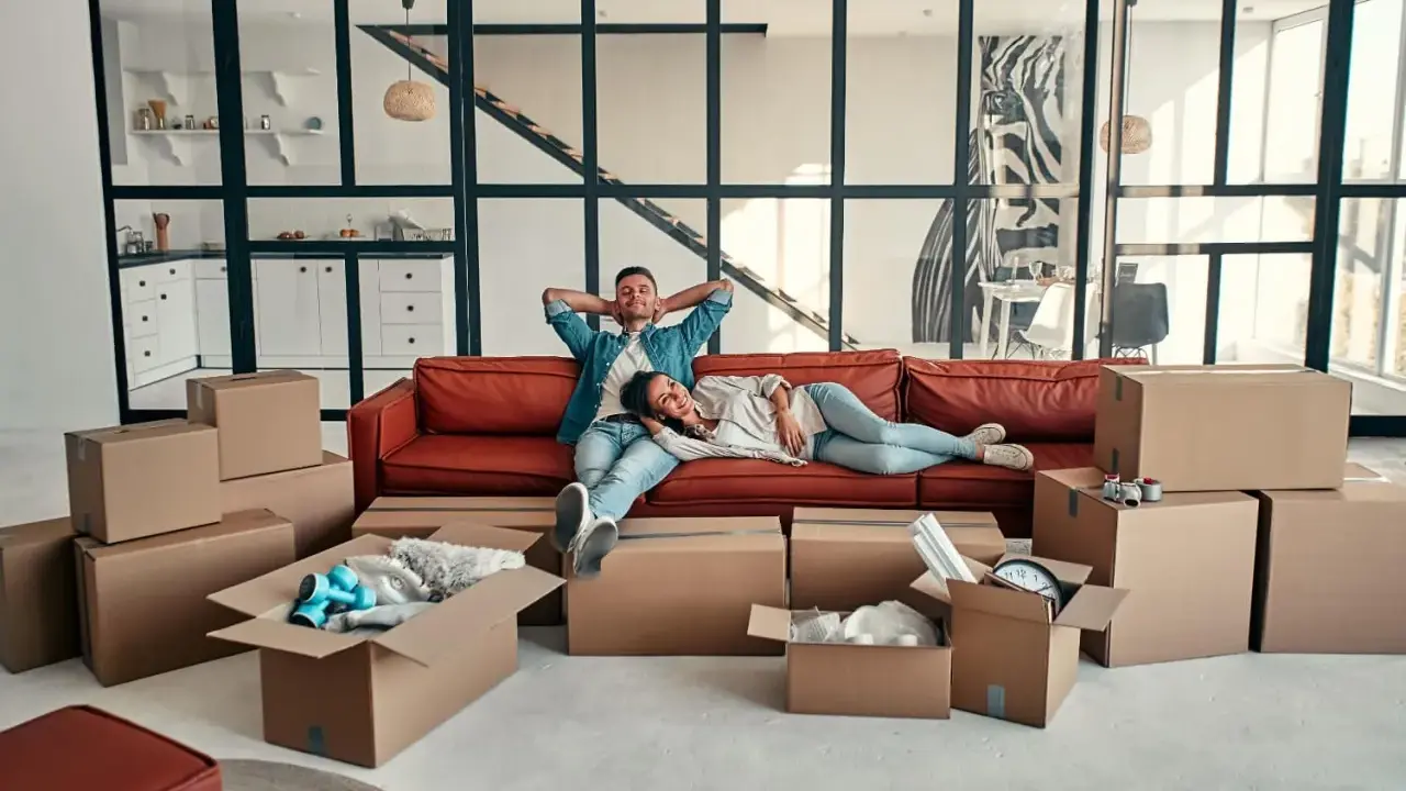 Couple se repose sur un canapé rouge entouré de cartons, signe d'un emménagement appartement réussi.