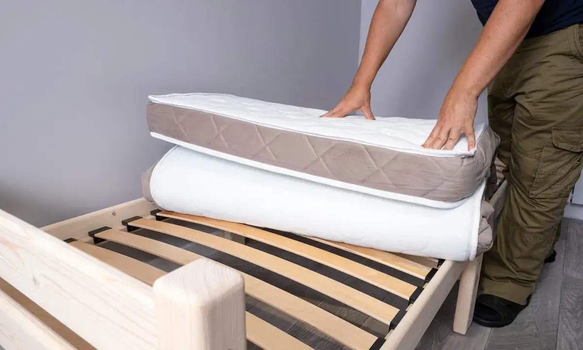 Un homme montre comment plier un matelas sur un sommier en bois.