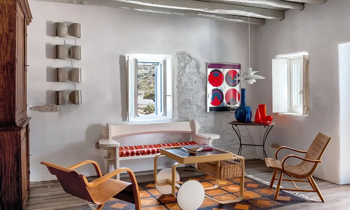 Salon d'une typique maison grecque avec mobilier en bois, tapis coloré et vue sur la mer par la fenêtre.