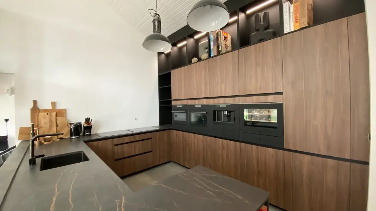 Cuisine moderne avec îlot central, plan de travail en marbre noir veiné, meubles en bois, électroménagers intégrés. L'implantation cuisine est pensée pour l'efficacité.