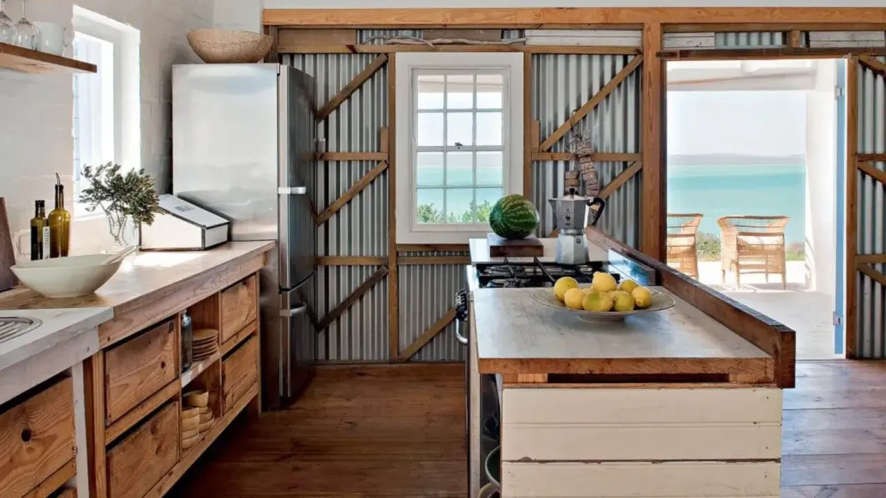 Cuisine campagne chic avec réfrigérateur, plan de travail en bois brut, murs en tôle ondulée et vue sur la mer.