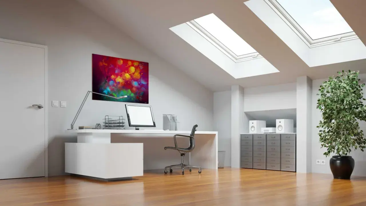 Bureau sous pente lumineux avec tableau abstrait coloré, ordinateur, plante verte et puits de lumière.