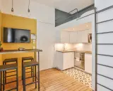 Aménagement studio 18m² : cuisine moderne, coin repas jaune vif avec TV, et lit mezzanine accessible par une échelle.