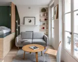 Aménagement intérieur appartement : un salon cosy avec canapé gris, table basse en bois, et un lit surélevé dans un coin.