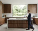 Cuisine moderne en 2 parties, avec des armoires en bois de noyer et un îlot central en marbre. Une grande fenêtre donne sur un jardin luxuriant.