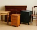 Un petit meuble en bois orange, une commode sombre et une chaise courbée, prêts à être relookés.