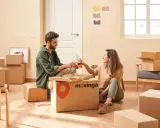 Un couple trinque avec des bouteilles devant une pizza, entouré de cartons. Un avis positif pour Movinga.