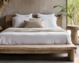 Lit de bois brut, draps blancs immaculés et coussin texturé créent une ambiance de parental chambre boheme chic. Une plante verte apporte une touche de nature.