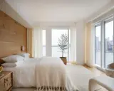Une chambre à coucher simple et moderne avec un mur en bois, un lit blanc douillet et une vue imprenable sur la ville et l'eau.