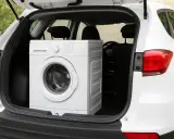 Un lave-vaisselle blanc est chargé dans le coffre d'une voiture blanche. On se demande si on peut coucher un lave-vaisselle pour le transporter.